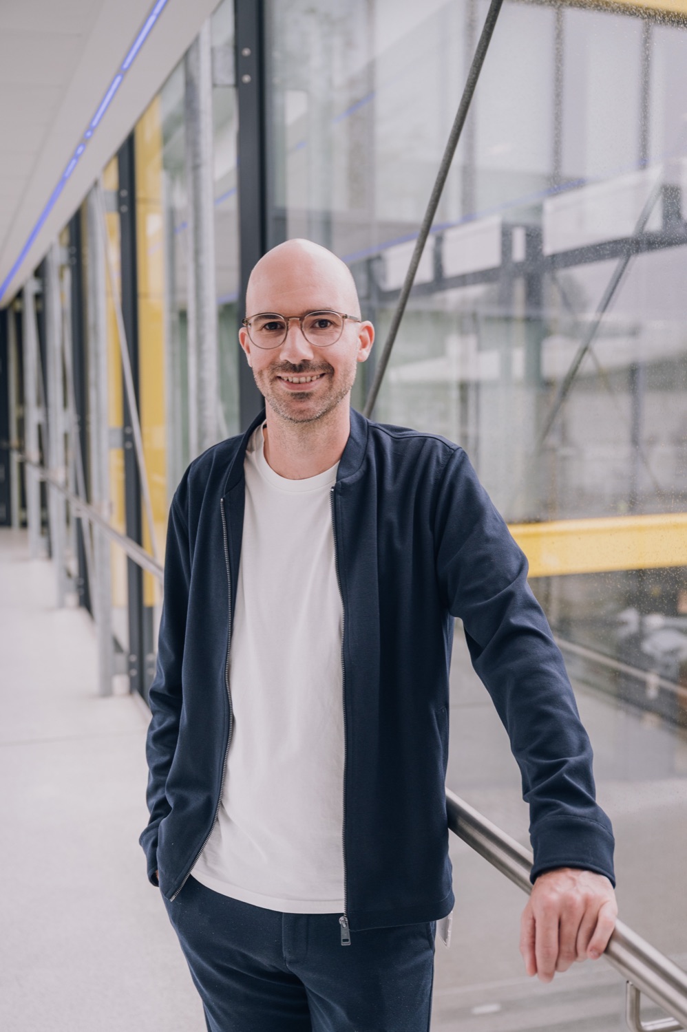Christopher Köster lehnt lächelnd an einem Geländer in einem lichtdurchfluteten Gang