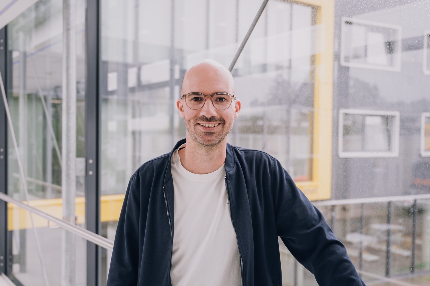 Christopher Köster steht in einem verglasten Gang mit gelben Akzenten