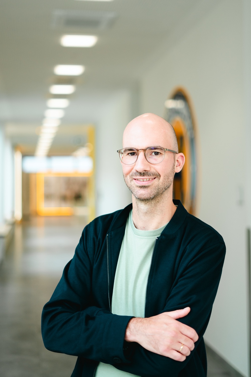 Christopher Köster mit verschränkten Armen in einem hellen Bürogang